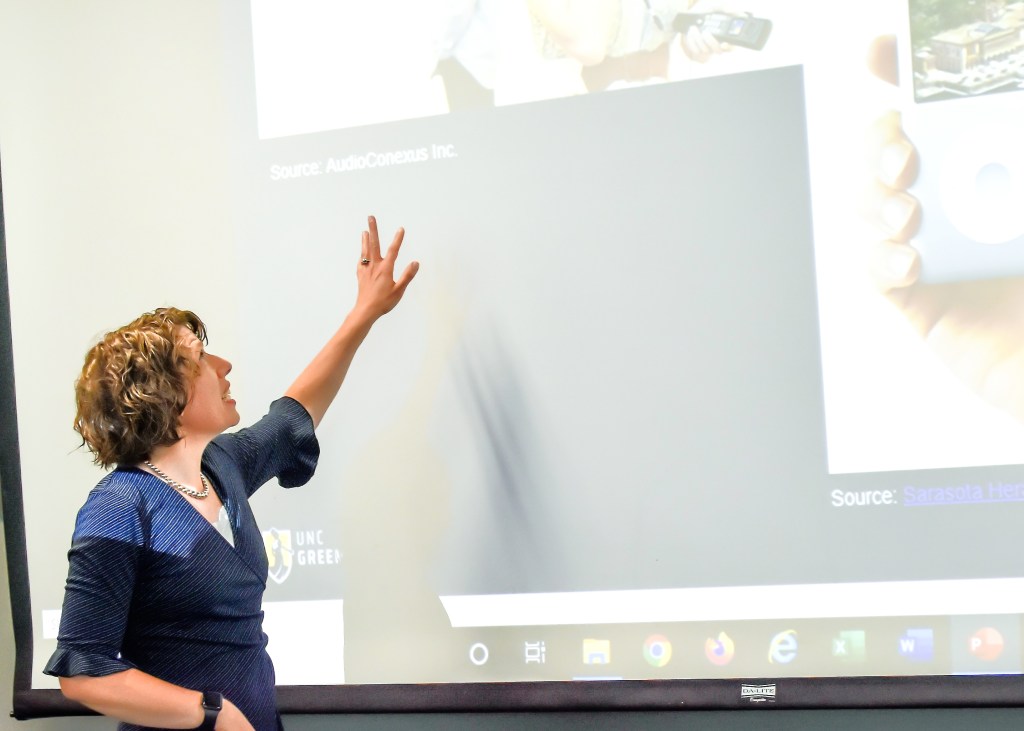 Hannah Grannemann gesturing to a screen with an arts management course presentation on it.